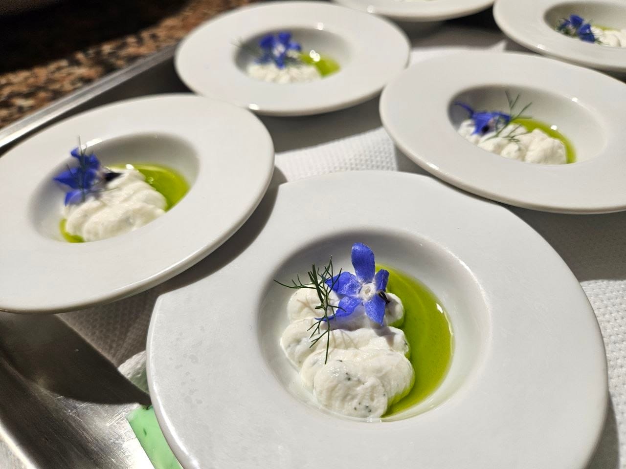 Dettaglio di un piatto gourmet: crema di formaggio, olio al basilico e fiore di borragine